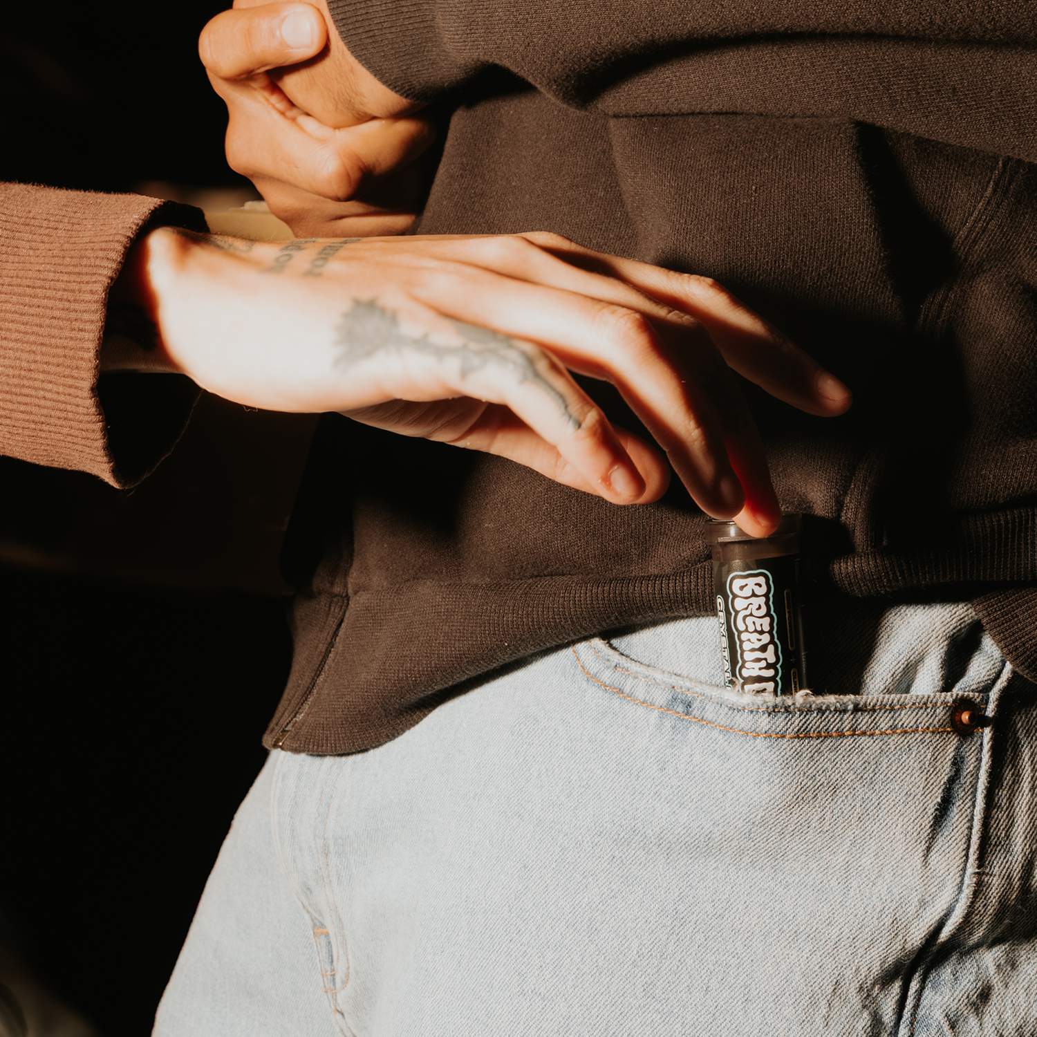 Close-up of a person wearing a brown hoodie and light blue jeans with a visible brand logo.